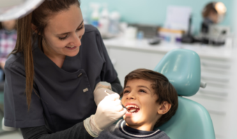 A dental assistant holds a dental mirror in the mouth of a child patient.